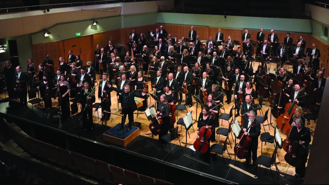 NSO - Full orchestra in concert dress standing for an ovation with conductor Jaime Martín on podium with arms outstretched