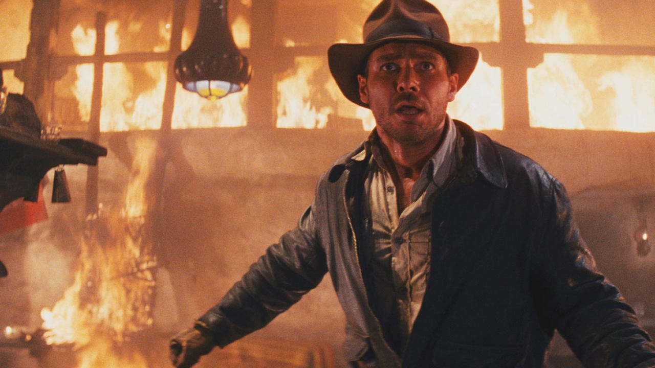 Still image from Raiders of the Lost Ark film with Harrison Ford - a man dressed in a leather jacket against a fire backdrop