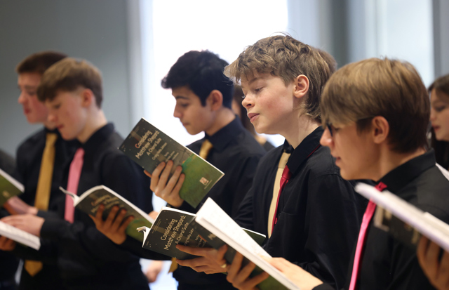 Cór Linn - young male members of the choir singing holding a songbook