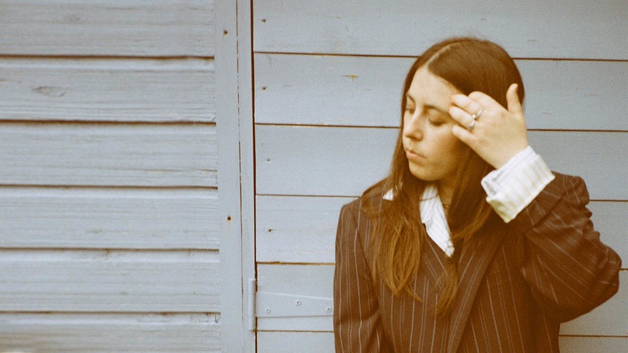 Sorcha - out of focus close-up of a woman in a pinstripe suit against a grey fence