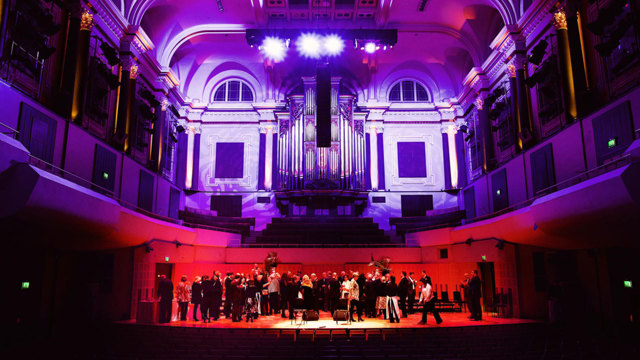 Wide shot of men and women on stage at NCH with pink and purple lighting