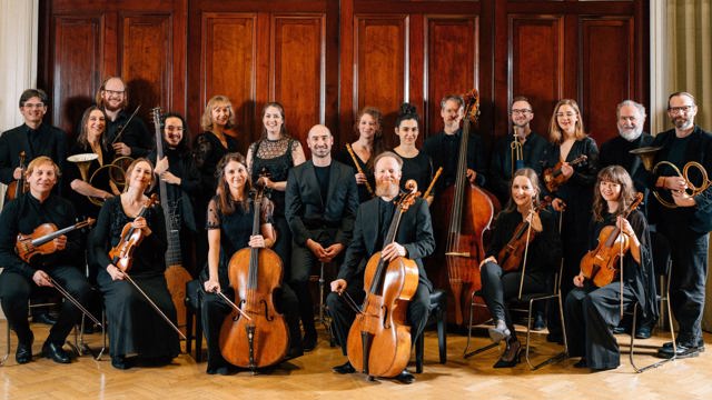 Wide image of Irish Baroque Orchestra musicians against a brown door backdrop