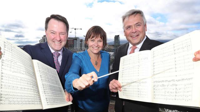 Paul Jacob of Grant Thornton; Alice Farnham, conductor & Sean McGrath, Allianz holding music scores & conductor's baton looking directly at the camera