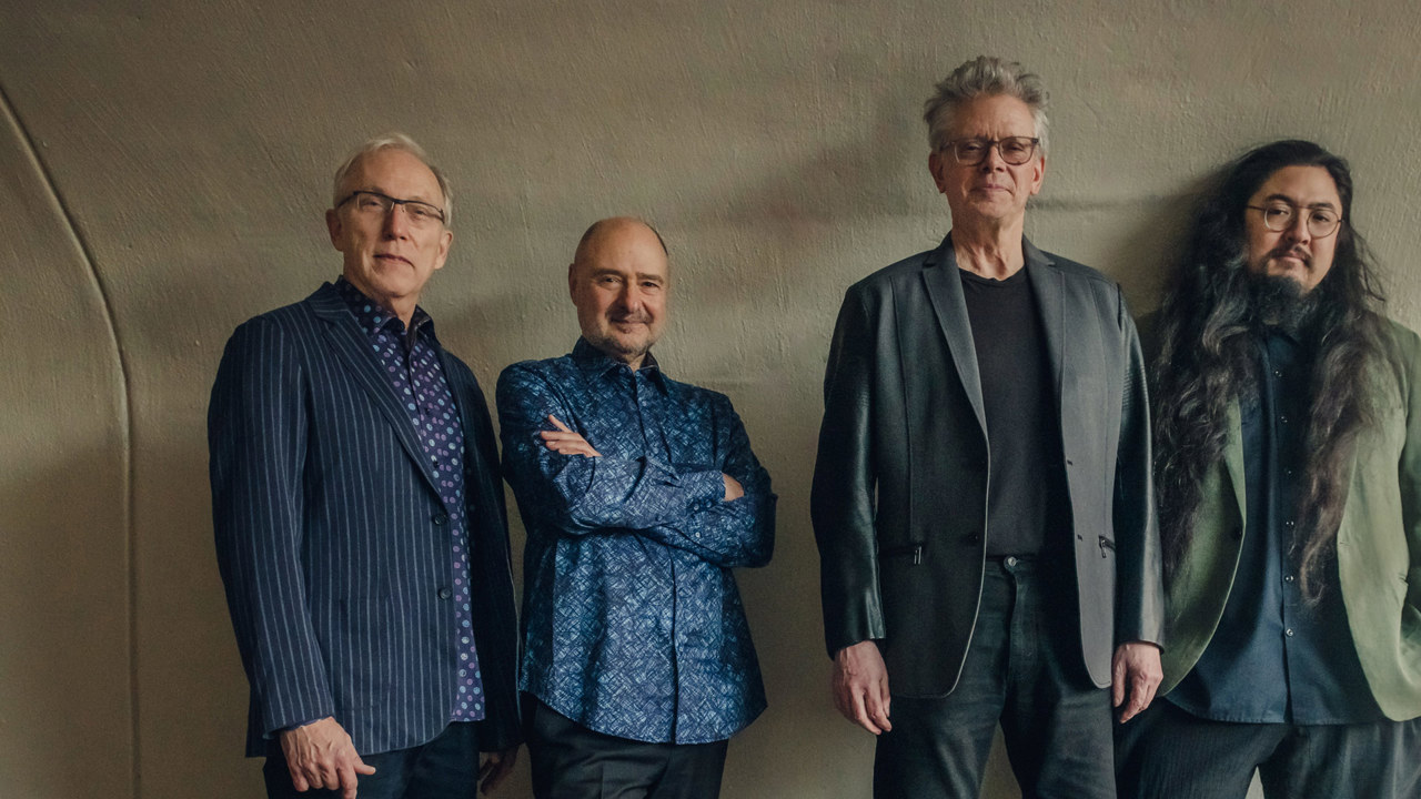 Kronos Quartet - four men posing against a beige wall looking directly at the camera